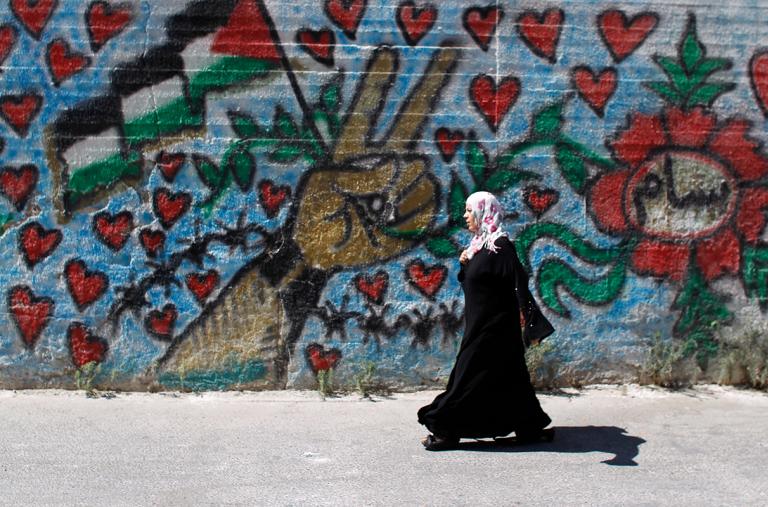 A Palestinian woman walks by a mural in Bethlehem