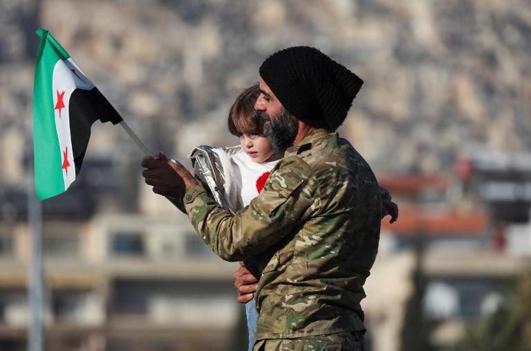 A man holds his child and a flag of the new Syrian regime in Damascus after the fall of the Assad government in 2024 - source: Reuters