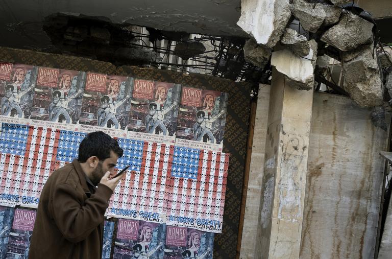 A man speaks on his phone in Beirut, Lebanon, in front of posters depicting the U.S. flag - source: Reuters