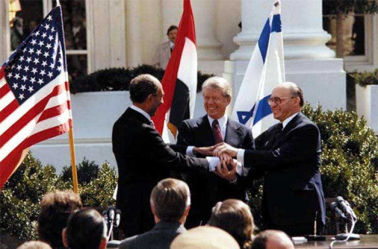 President Jimmy Carter, Egyptian President Anwar Sadat, and Israeli Prime Minister Menachem Begin shake hands at the White House as the Camp David Accords are announced.