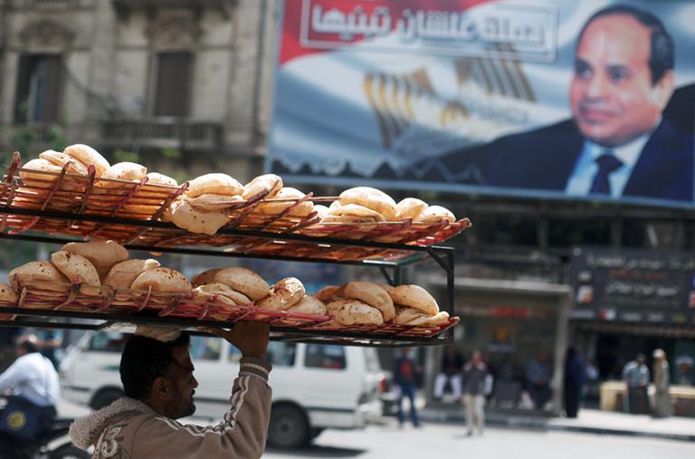 A bread seller in Cairo walks past a sign promoting President Sisi - source: Reuters