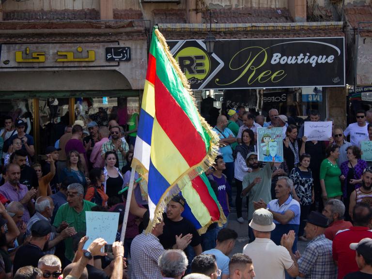 Protesting Syrians in the town of Suwayda hold signs and Druze flags - source: Reuters