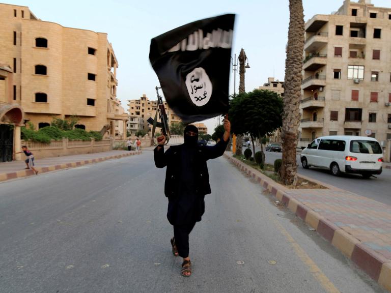 An Islamic State fighter waves an ISIS flag while brandishing an automatic rifle in Raqaa, Syria - source: Reuters