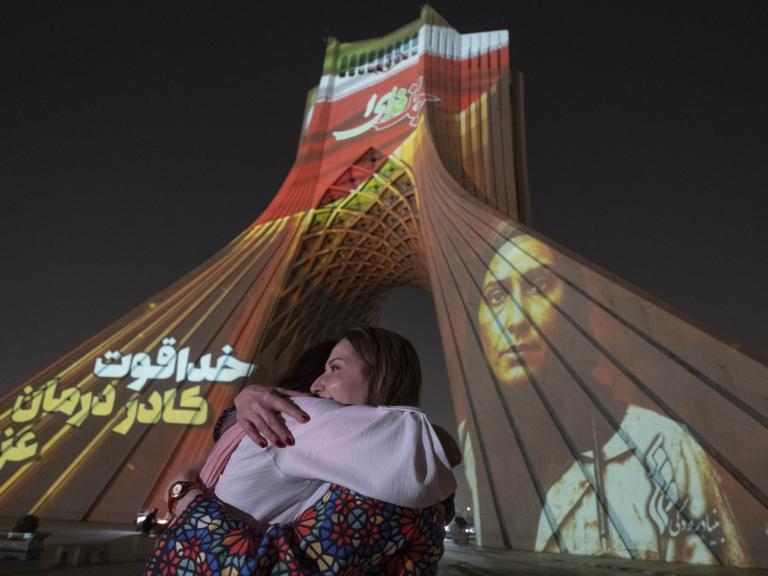 Two Iranian women hug each other while a country's flag and a portrait of an Iran-Israel war victim are projected on the Azadi (Freedom) Monument in western Tehran, Iran, on June 25, 2025 - source: Reuters