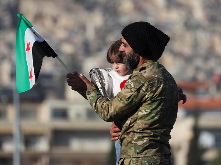 A man holds his child and a flag of the new Syrian regime in Damascus after the fall of the Assad government in 2024 - source: Reuters