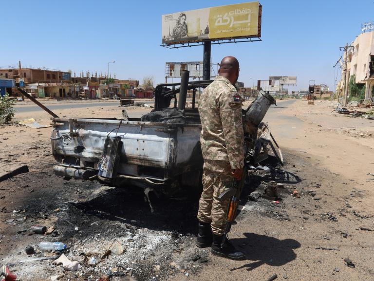 A Sudanese army soldier stands near a bombed-out vehicle outside Khartoum - source: Reuters