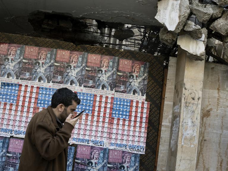 A man speaks on his phone in Beirut, Lebanon, in front of posters depicting the U.S. flag - source: Reuters