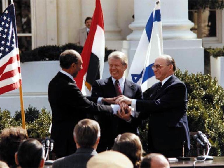 President Jimmy Carter, Egyptian President Anwar Sadat, and Israeli Prime Minister Menachem Begin shake hands at the White House as the Camp David Accords are announced.