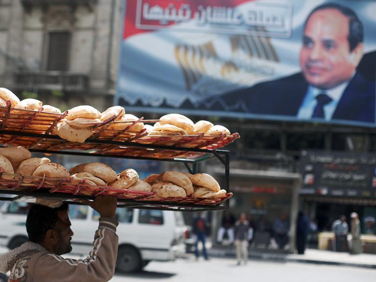 A bread seller in Cairo walks past a sign promoting President Sisi - source: Reuters