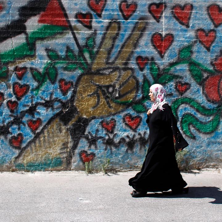 A Palestinian woman walks by a mural in Bethlehem