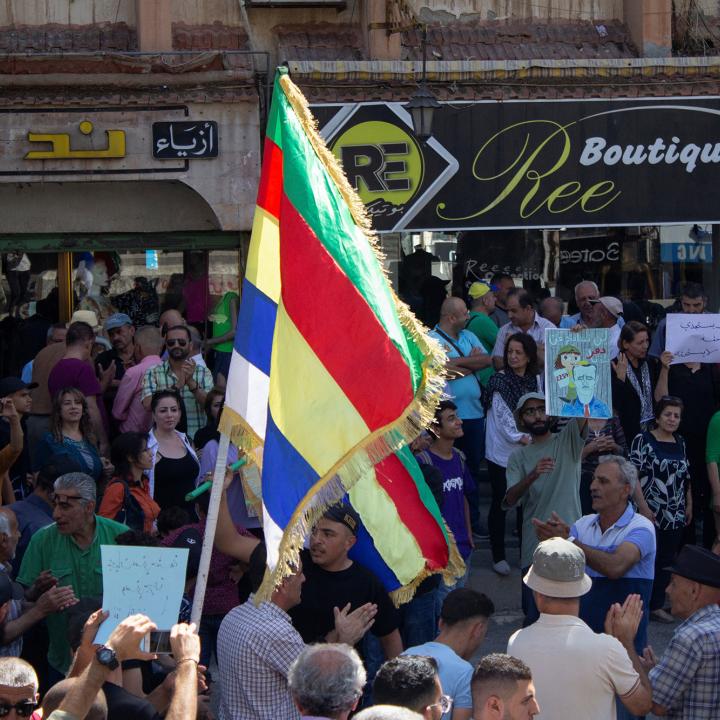 Protesting Syrians in the town of Suwayda hold signs and Druze flags - source: Reuters