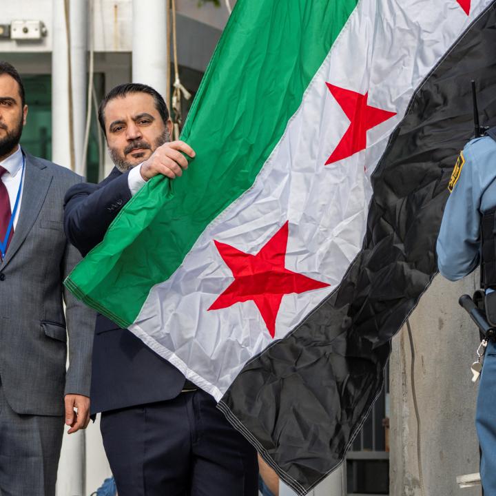 Photo of Syrian Foreign Minister Assad al-Shaibani next to the national flag.