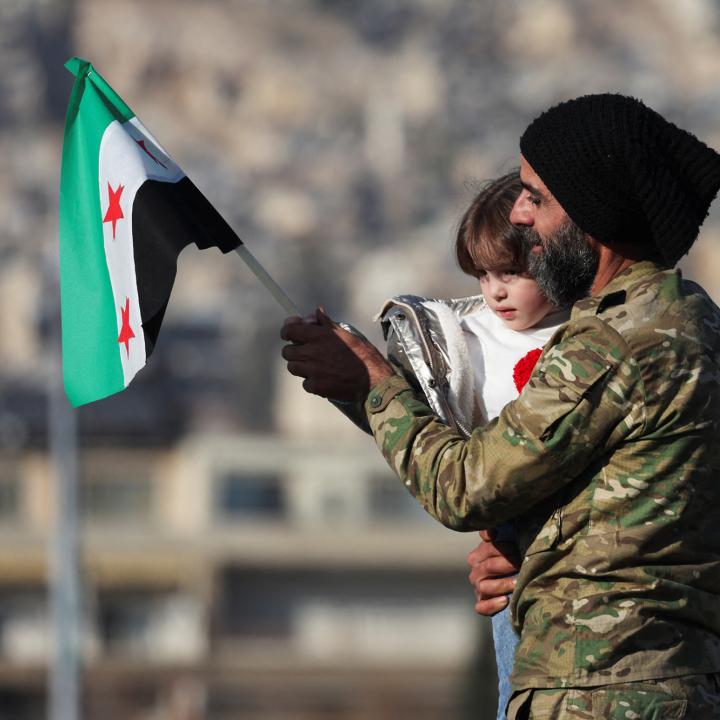 A man holds his child and a flag of the new Syrian regime in Damascus after the fall of the Assad government in 2024 - source: Reuters