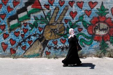 A Palestinian woman walks by a mural in Bethlehem