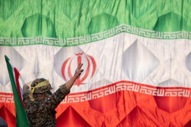 An Iranian soldier wearing an IRGC uniform salutes in front of an Iranin flag - source: Reuters