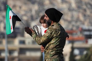 A man holds his child and a flag of the new Syrian regime in Damascus after the fall of the Assad government in 2024 - source: Reuters