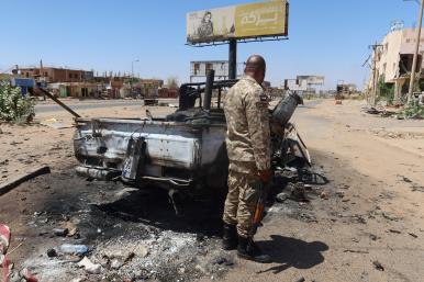 A Sudanese army soldier stands near a bombed-out vehicle outside Khartoum - source: Reuters