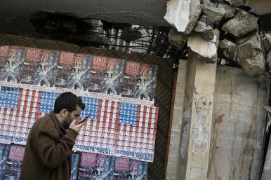 A man speaks on his phone in Beirut, Lebanon, in front of posters depicting the U.S. flag - source: Reuters