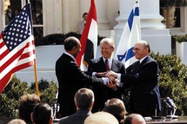 President Jimmy Carter, Egyptian President Anwar Sadat, and Israeli Prime Minister Menachem Begin shake hands at the White House as the Camp David Accords are announced.