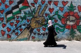 A Palestinian woman walks by a mural in Bethlehem