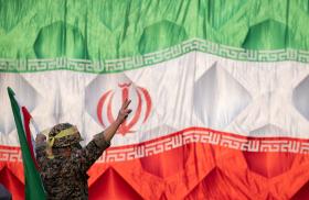 An Iranian soldier wearing an IRGC uniform salutes in front of an Iranin flag - source: Reuters