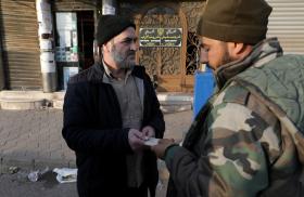 A fighter from Syria's de-facto post-Assad government checks a civilian's identity documents after a curfew was imposed in the Alawite-majority city of Homs in December 2024 - source: Reuters