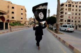 An Islamic State fighter waves an ISIS flag while brandishing an automatic rifle in Raqaa, Syria - source: Reuters