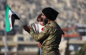 A man holds his child and a flag of the new Syrian regime in Damascus after the fall of the Assad government in 2024 - source: Reuters