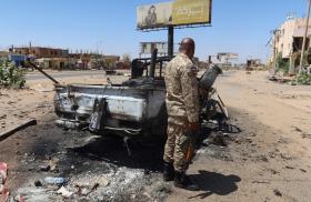 A Sudanese army soldier stands near a bombed-out vehicle outside Khartoum - source: Reuters