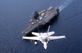 A U.S. Navy F-18 flies above a carrier - source: Department of Defense
