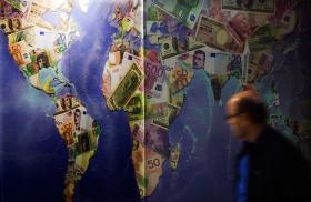 A man walks by a mural of international currencies